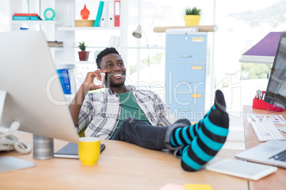 Male executive talking on mobile phone while relaxing at his desk in office