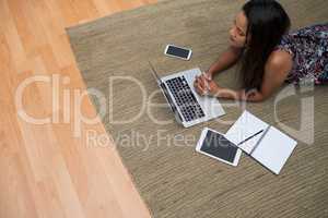 Female executive using laptop while lying on carpet