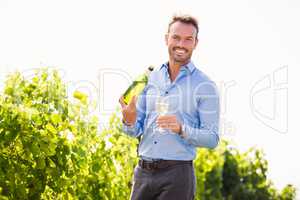 Portrait of smiling young man holding wine bottle and glass