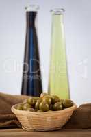 Close up of green olives in wicker basket by oil bottles