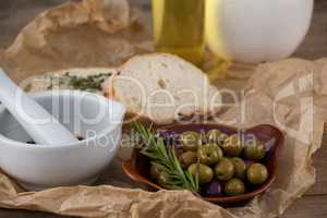 Mortar pestle by olives in plate on paper