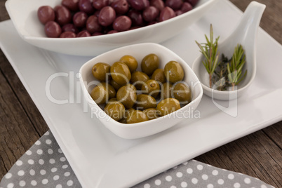 Green and brown olives in bowls by rosemary