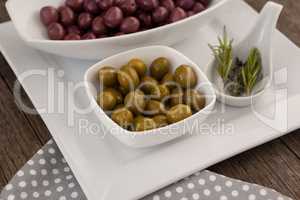 Green and brown olives in bowls by rosemary