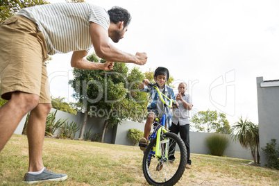 Father and grandfather cheering for boy cycling in yard