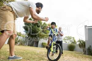 Father and grandfather cheering for boy cycling in yard