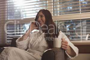 Woman talking on mobile phone while having coffee in the living room