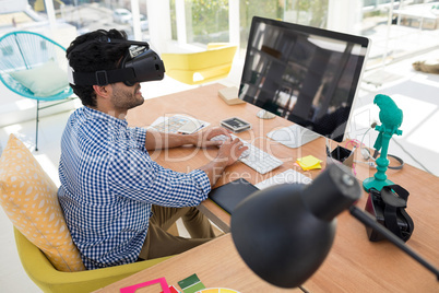 Graphic designer in virtual reality headset working on computer at desk