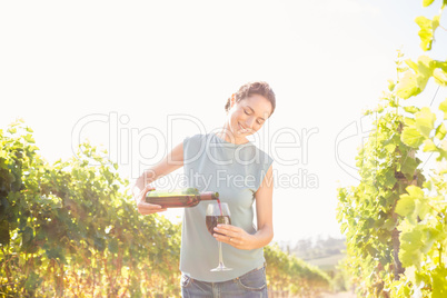 Woman pouring wine from bottle in glass on sunny day