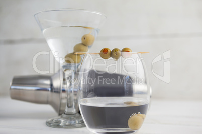 Close up of green olives in vodka martini with cocktail shaker