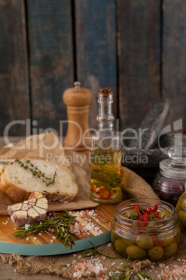 Ingredients with olives in container by bread on cutting board