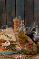 Ingredients with olives in container by bread on cutting board