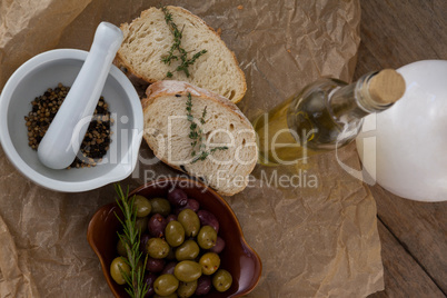 Directly above shot of olives with oil bottle and bread by spices in mortar pestle on crumbled paper