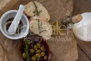 Directly above shot of olives with oil bottle and bread by spices in mortar pestle on crumbled paper