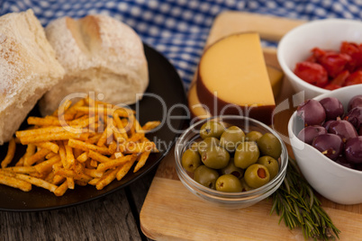 French fries with bread by olives and vegetables on cutting board