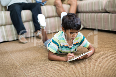 Boy using tablet while lying on carpet with father and grandfather in background