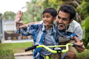 Father and son waving hand while cycling