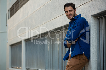 Smiling young man with arms crossed leaning on wall