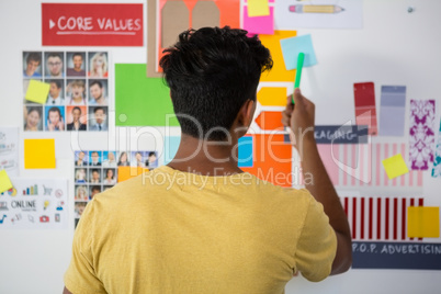 Rear view of man pointing at sticky note in office