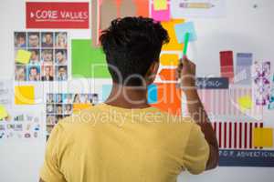 Rear view of man pointing at sticky note in office