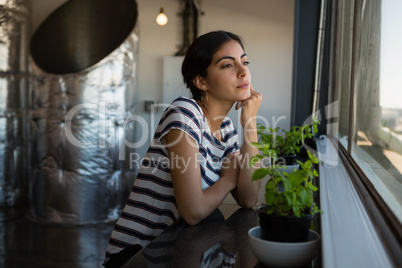Thoughtful young woman looking through window at office
