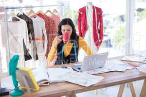 Female designer using laptop while having coffee