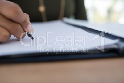 Female executive writing on a document at desk in the office