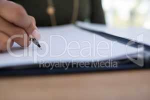 Female executive writing on a document at desk in the office