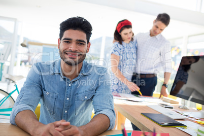 Male graphic designer relaxing while coworkers working in the office