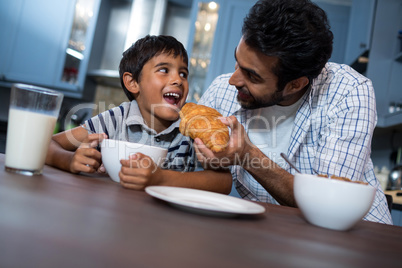 Smiling father feeding croissant to son