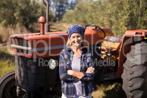 Portrait of happy woman standing with arms crossed against tractor