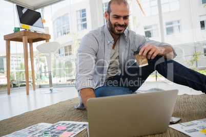 Smiling designer holding disposable cup using laptop