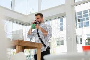 Businessman having drink while talking on mobile phone while standing at desk