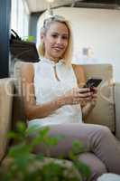 Portrait of smiling woman using phone on sofa at office