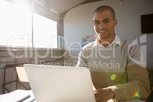 Portrait of man using laptop at office on sunny day