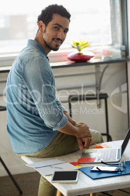 Portrait of man sitting on desk in office