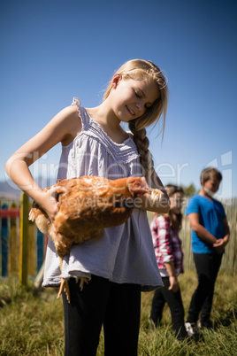 Smiling girl carrying a hen in the farm
