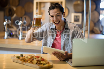 Smiling man holding beer mug and digital tablet in restaurant