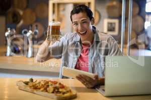 Smiling man holding beer mug and digital tablet in restaurant