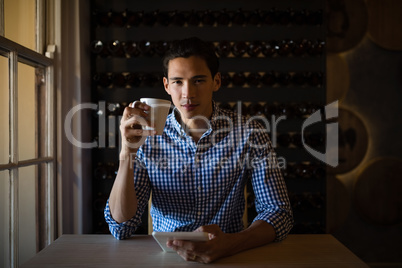 Man holding digital tablet and coffee cup in restaurant