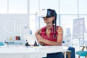 Female graphic designer in virtual reality headset using digital tablet at desk