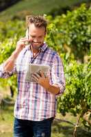 Man talking on phone while using tablet at vineyard