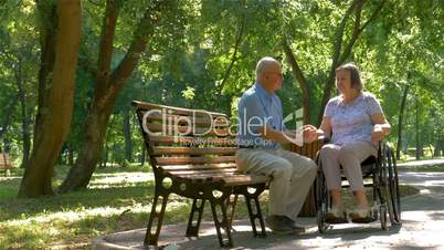 Senior man with woman in wheelchair outside in park
