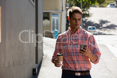 Young man using phone while walking by building