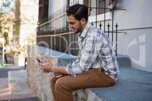 Man using mobile phone while sitting on retaining wall