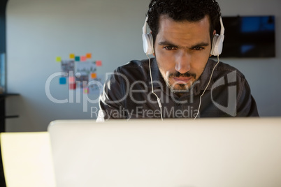 Businessman listening to headphones while using laptop