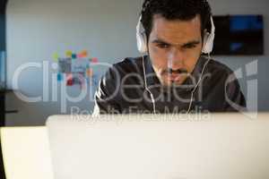 Businessman listening to headphones while using laptop