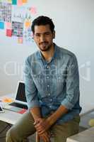 Portrait of man sitting on desk at office