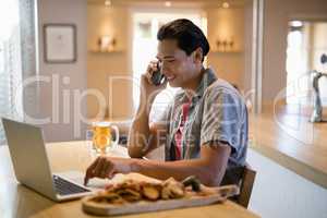 Man using laptop while talking on mobile phone in a restaurant