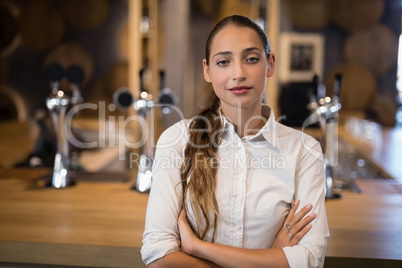 Female bartender standing with arms crossed in bar