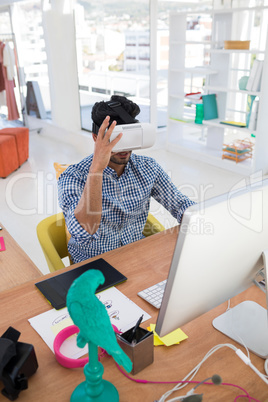 Graphic designer in virtual reality headset working on computer at desk